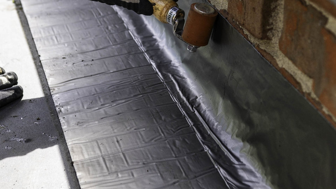 Supraseal tape being rolled into a roof-to-wall junction on a rubber membrane roof