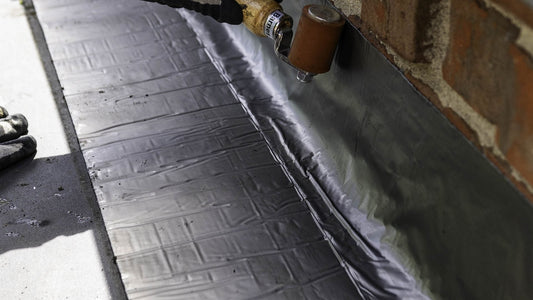 Supraseal tape being rolled into a roof-to-wall junction on a rubber membrane roof