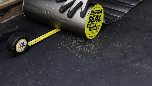 Roll of Supraseal tape being laid along a wall on a flat roof