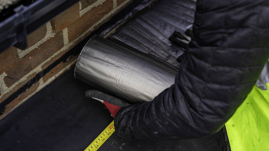 Roofer rolling out Supraseal flashing tape along a flat roof upstand