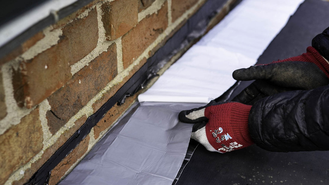 Supraseal flashing tape being pressed against brickwork at a flat roof upstand